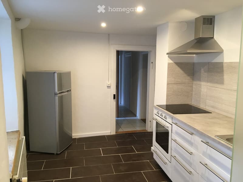 Modern kitchen with white cabinets, stainless steel appliances, dark tiled floor, and a doorway leading to another room.