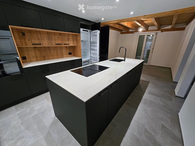 Modern kitchen with a white marble island, black cabinets, and stainless steel appliances. Features include a sink, faucet, and an open refrigerator.
