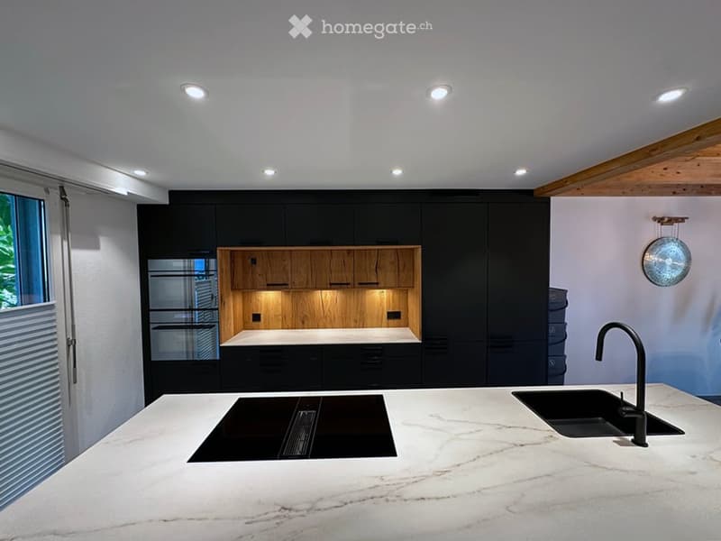 Modern kitchen with a white marble island, black cabinets, and a wooden accent section. Features include a sink, faucet, and integrated lighting.