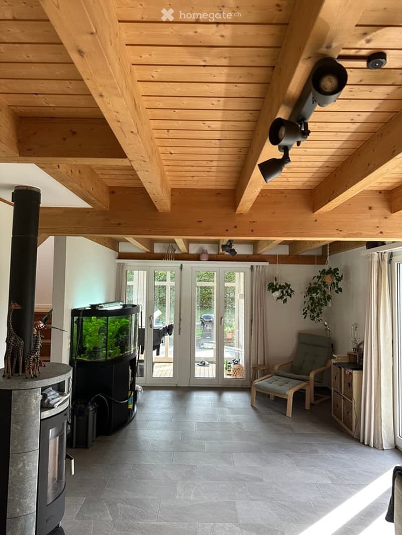 Bright living room with exposed wooden beams, a modern fireplace, aquarium, comfortable seating, and large glass doors leading to an outdoor area.
