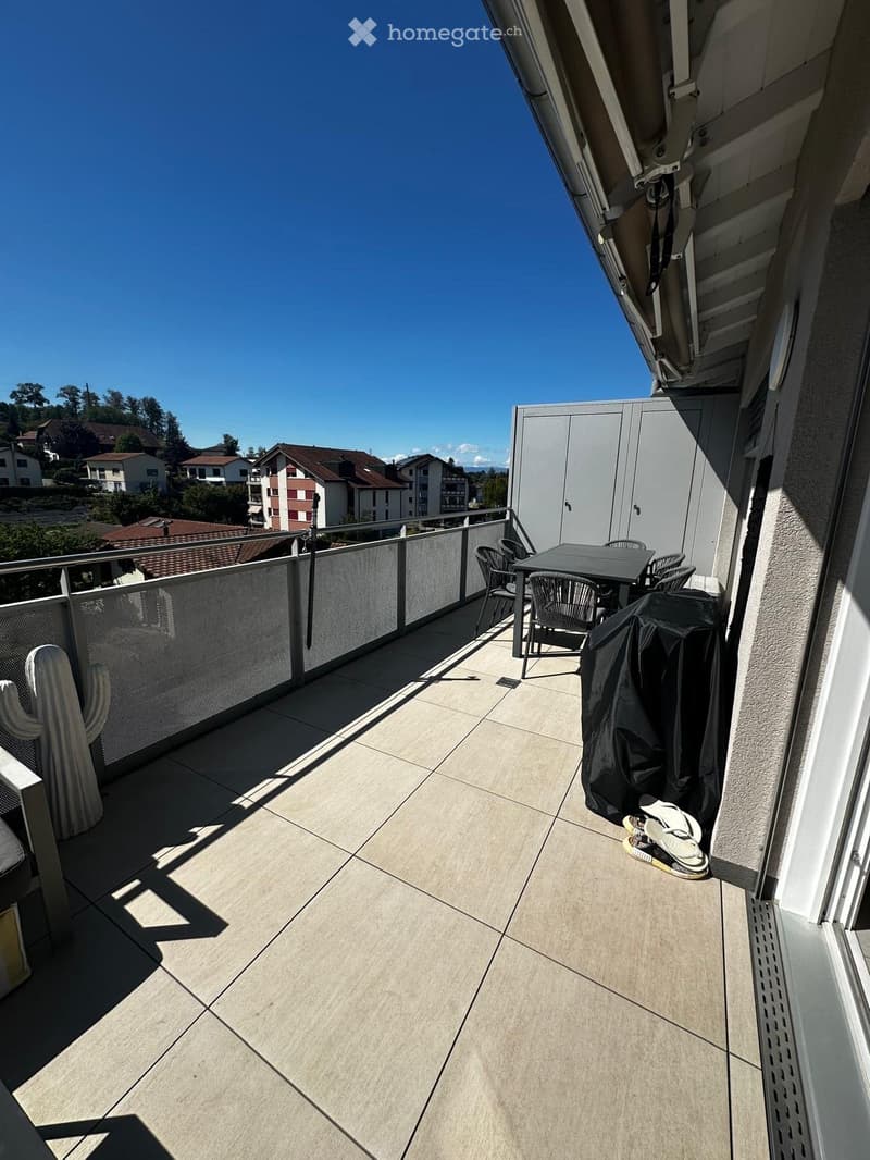 Balcony with tiled floor, metal railing, small table and chairs, covered grill, and a cactus plant.