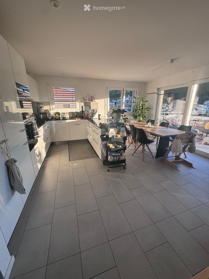 Modern kitchen with white cabinets, stainless steel appliances, a dining table with chairs, and a cart with various items.