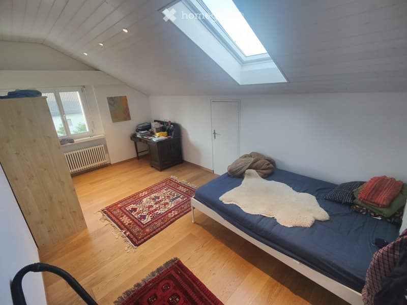 Bedroom with wooden flooring, a single bed with blue bedding, a white fur throw, a desk with a chair, a cabinet, and two rugs on the floor.