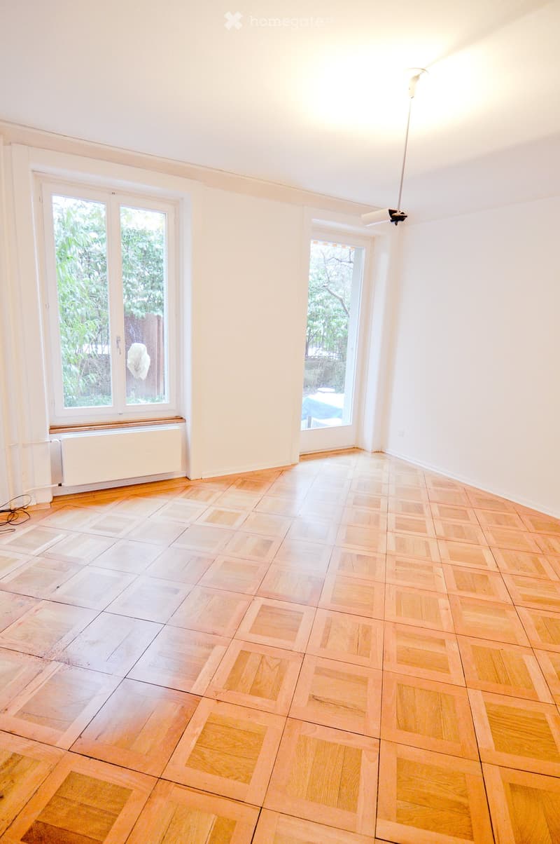 Empty room with wooden flooring, white walls, large windows, and a radiator. No furniture or equipment present.