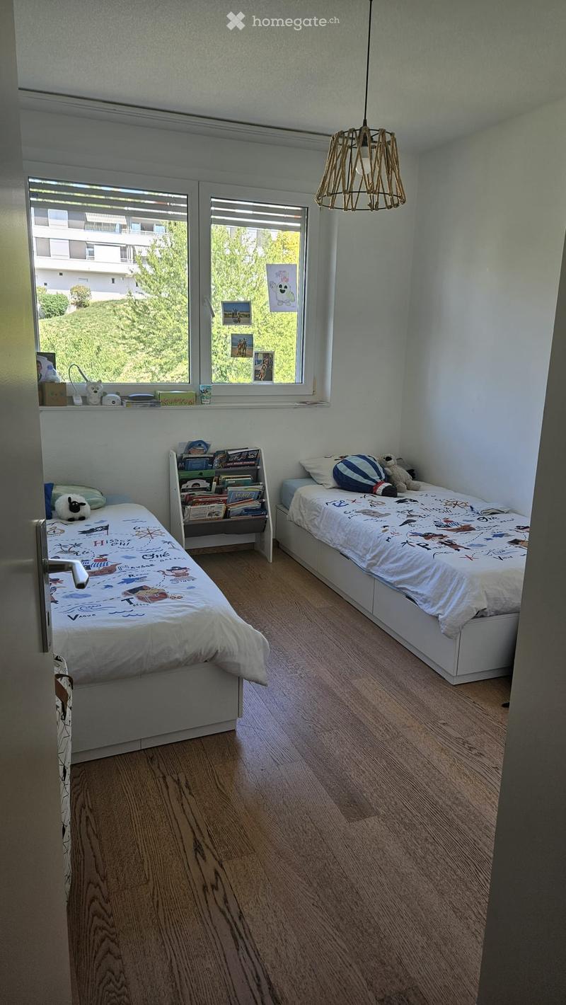 Cozy children's bedroom with two single beds, a bookshelf, and decorative items on the windowsill.