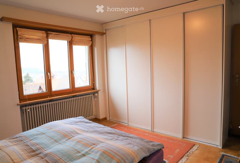 Bright bedroom with a double bed, a large wardrobe, and a window with blinds offering a view of the outdoor area.