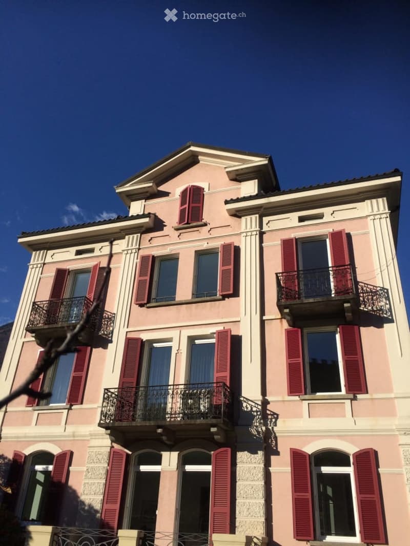 Pink building with multiple floors, red shutters, and balconies.