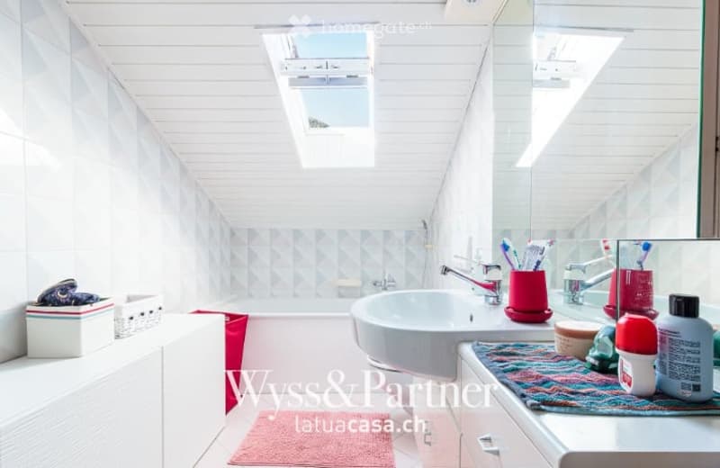 Bright, modern bathroom with white walls and ceiling, featuring a bathtub, sink, mirror, and various toiletries neatly arranged on the counter.
