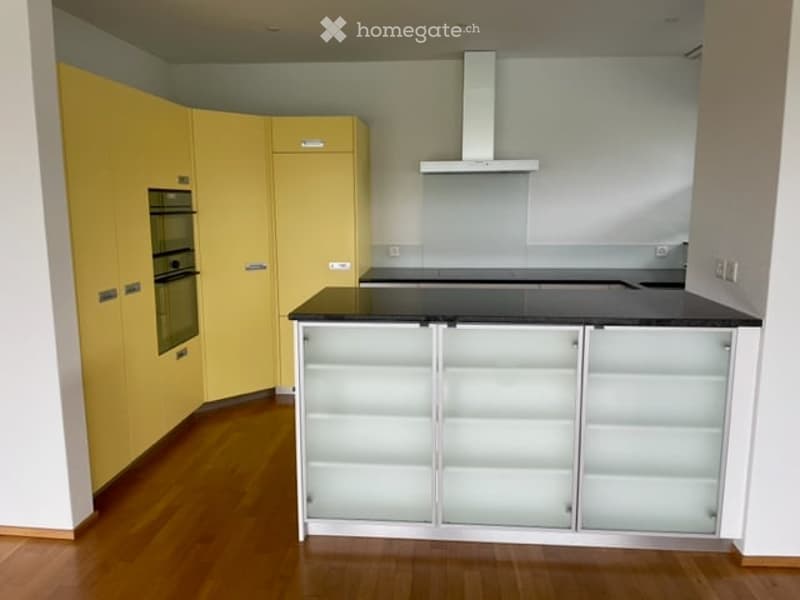 Modern kitchen with yellow cabinets, white countertops, and a central island with glass-fronted storage. Features an oven and a range hood.