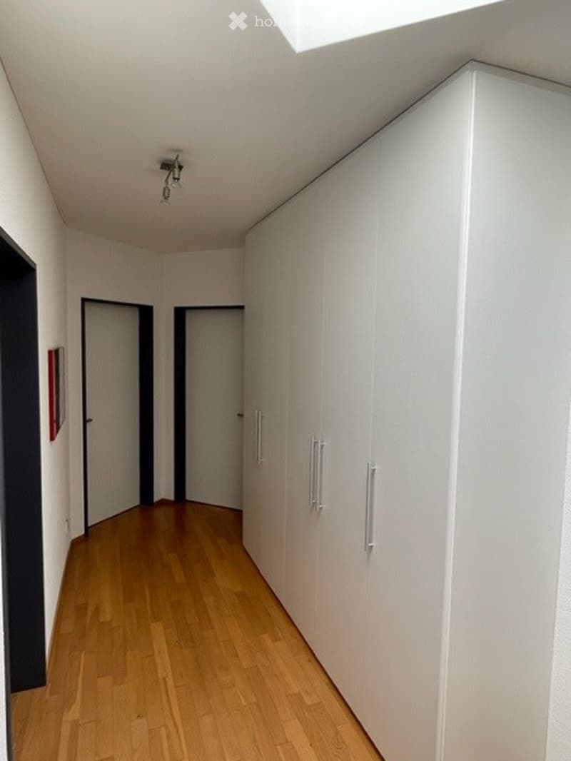 Empty hallway with wooden flooring, white walls, built-in white cabinets, and two doors at the end.