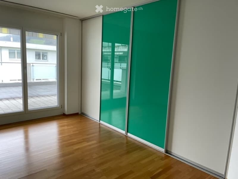 Empty room with wooden flooring, large glass sliding doors leading to a balcony, and a green sliding closet.