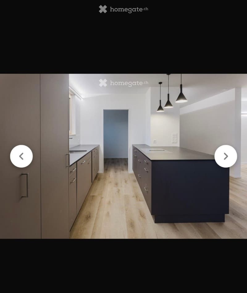 Modern kitchen with light wooden flooring, dark cabinets, and a central island with a countertop and sink.