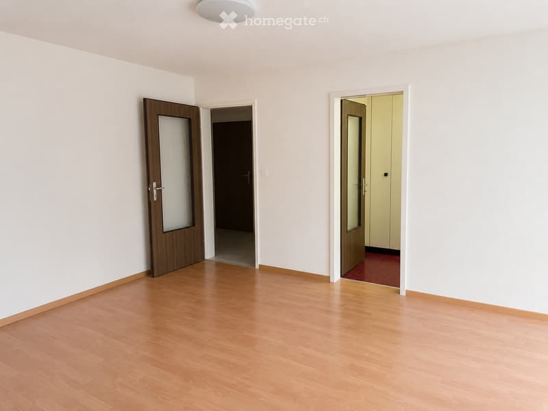 Empty room with light wooden flooring, white walls, and two open doors leading to other spaces.