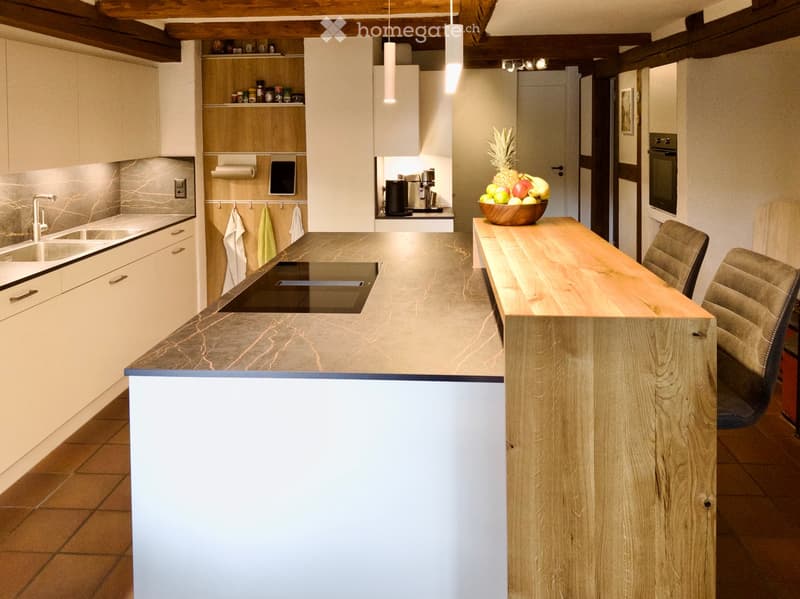 Modern kitchen with white cabinets, marble countertop, stainless steel sink, and a wooden island with seating. Includes a bowl of fruit on the island.