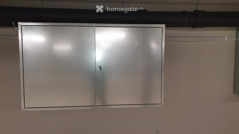 Empty room with a metallic cabinet mounted on a plain wall. No furniture or equipment visible.