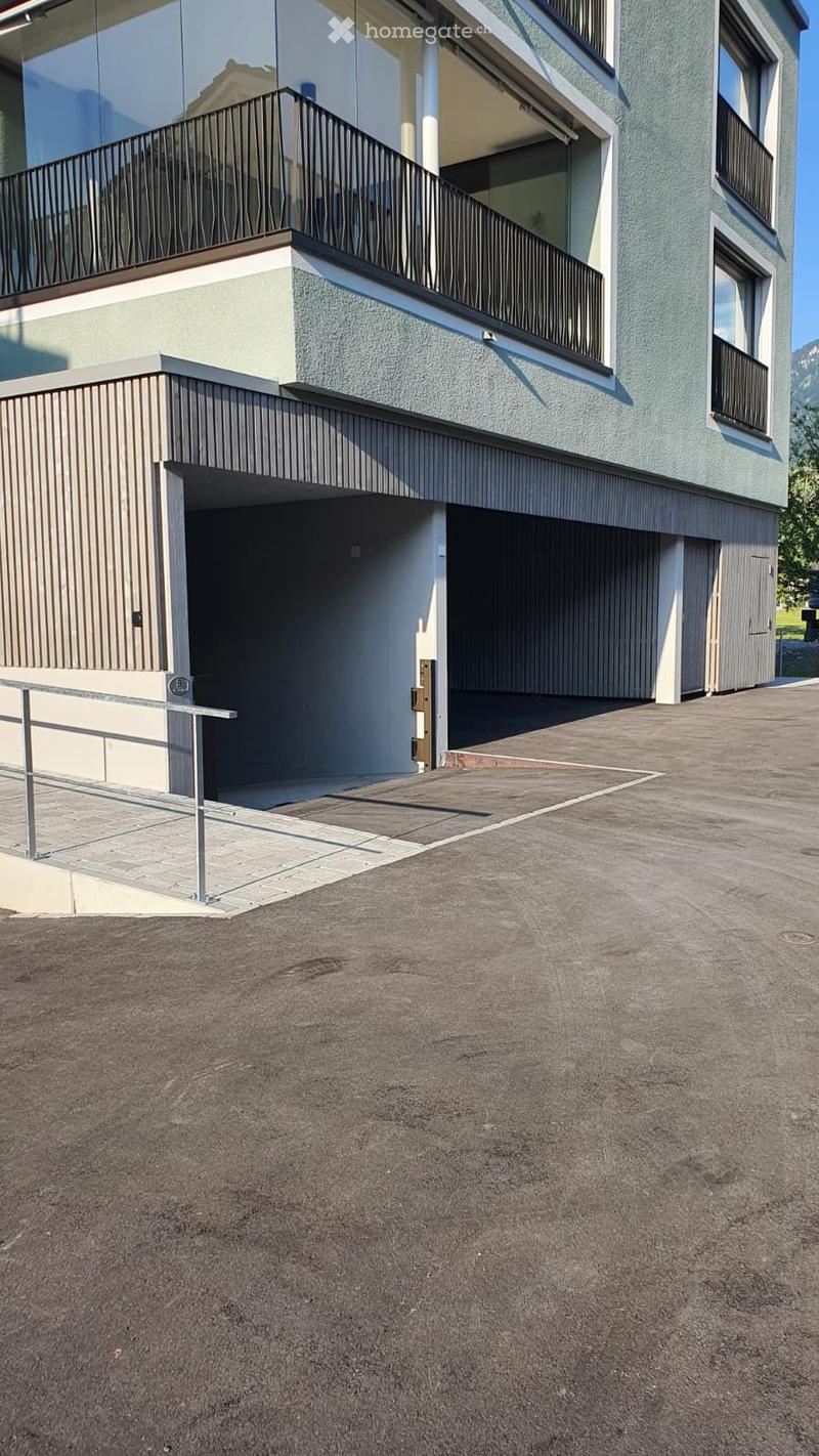 Modern two-story building with a balcony, garage, and raised ground floor entrance.