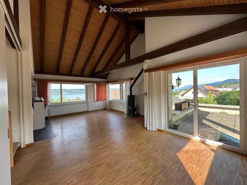 Bright, open room with wooden floors, large windows, and a view of the lake and mountains. Features a fireplace and sliding glass doors leading to a balcony.