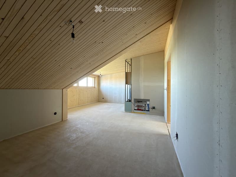 Empty attic space with wooden slatted ceiling, concrete walls, and a small window letting in natural light. Exposed electrical panel and wiring visible.