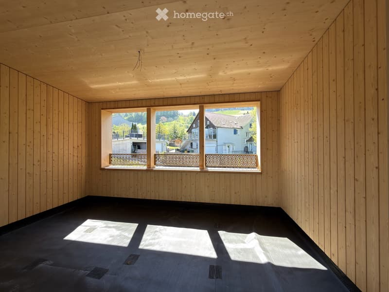 An empty room with wooden walls and ceiling, large windows with metal railings, and a dark floor.