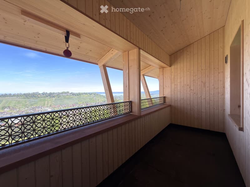 Wooden balcony with large windows offering a scenic view of a valley and town below.