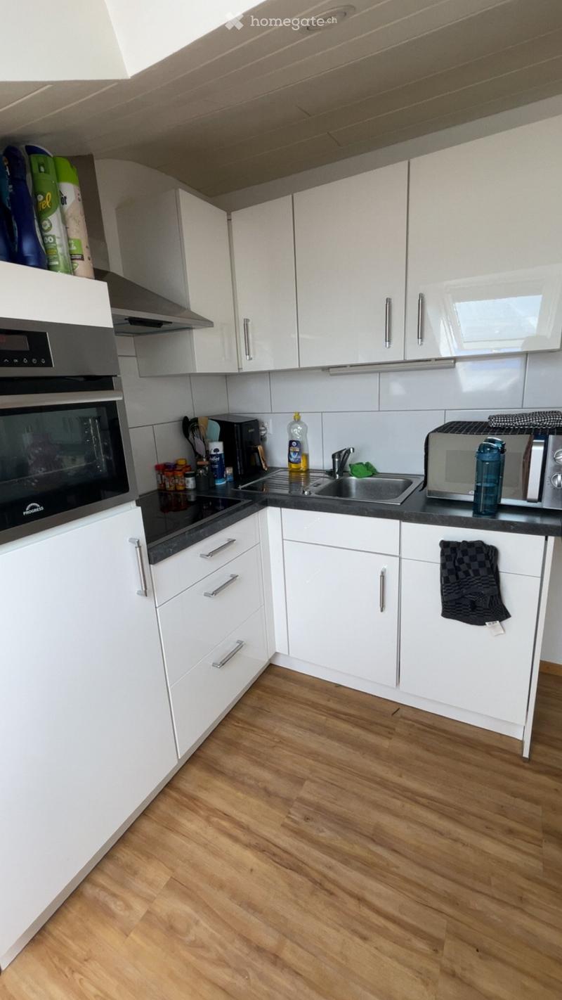 Modern kitchen with white cabinets, black countertops, and wooden flooring. Includes an oven, microwave, sink, and various small appliances.