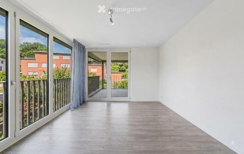 Empty room with large windows, wooden flooring, and a sliding door leading to a balcony.