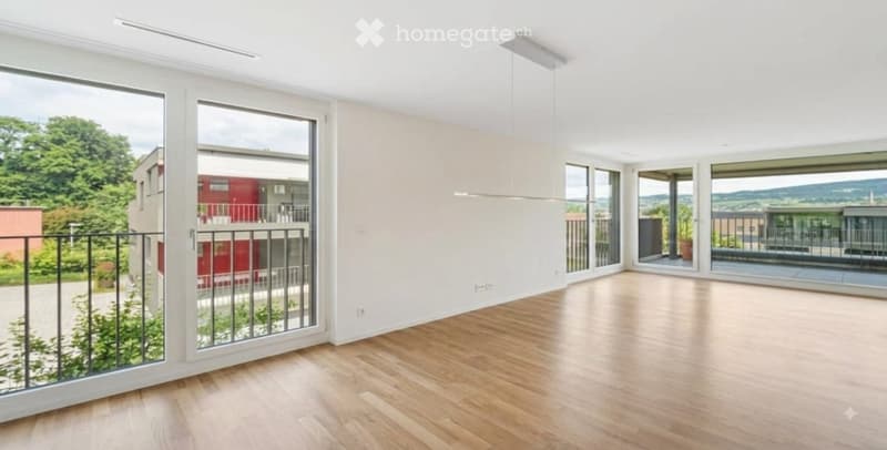 Bright, empty room with wooden flooring, large windows, and sliding glass doors leading to a balcony.