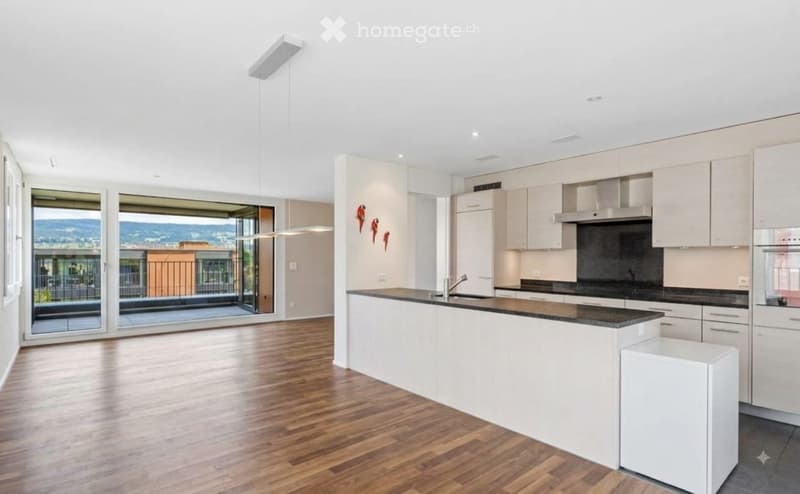Modern kitchen with white cabinets, a central island, and a view of the balcony and surrounding landscape.