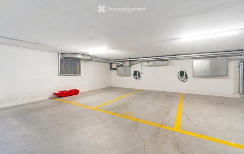 {"type": "Garage", "objects": ["electric vehicle charger", "storage box"], "description": "Clean, well-lit underground garage with concrete floor, yellow parking lines, two electric vehicle charging stations, and a red storage box.", "localized_descriptio