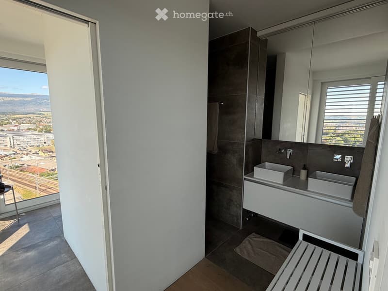 Modern bathroom with double sink, large mirror, and a view of the cityscape through large windows.