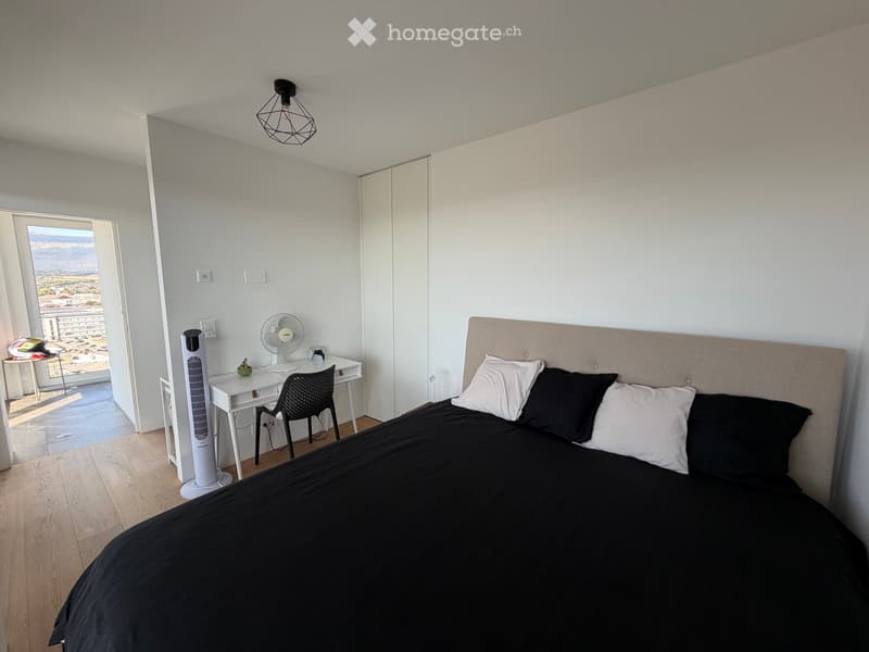 Modern bedroom with a large bed, desk, chair, and fan. Offers a scenic view through an open door.