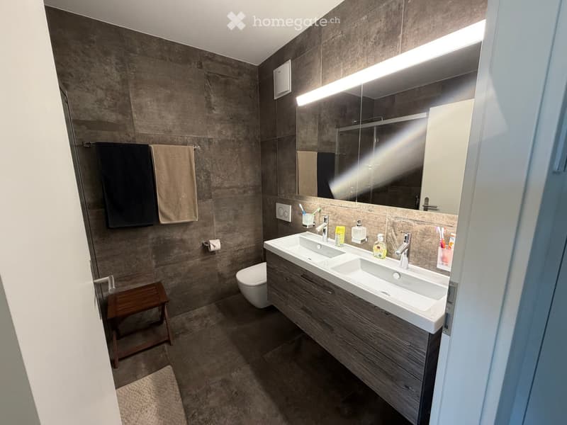 Modern bathroom with double sink, wooden vanity, large mirror, toilet, and towels.