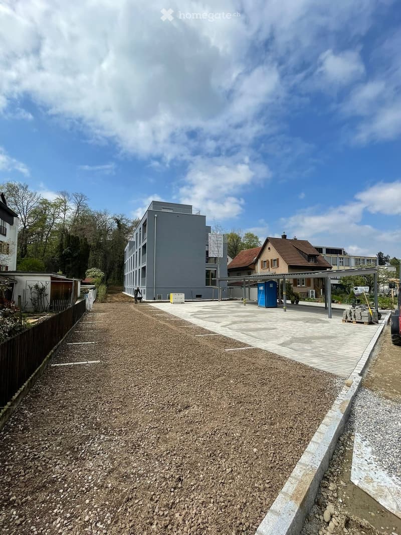 apartment building under construction, parking area with carport, large concrete sidewalk