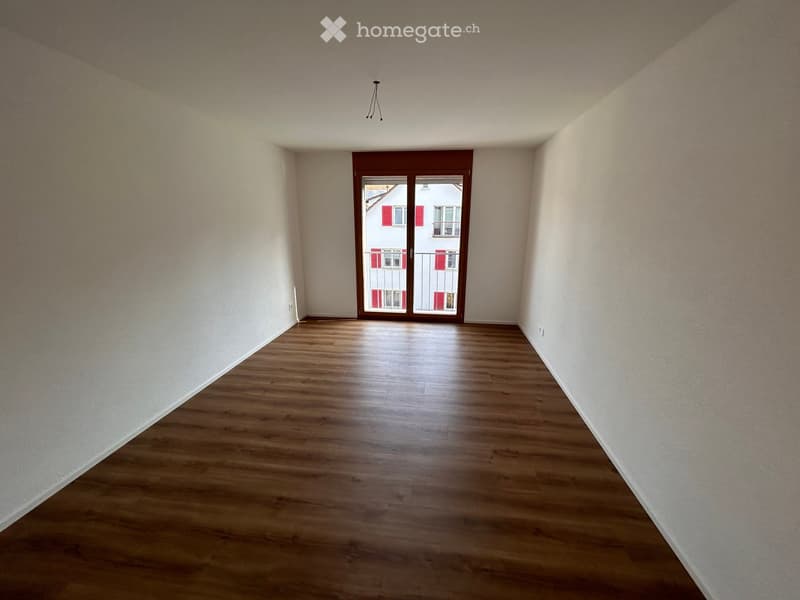 empty room with wooden floors, white walls, sliding glass doors leading to a balcony with a view of a building