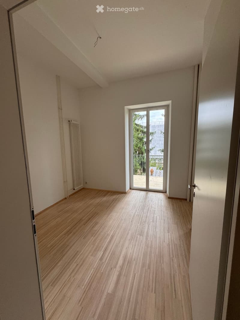 Empty room with wooden flooring, light-colored walls, and a sliding glass door leading to a balcony area.