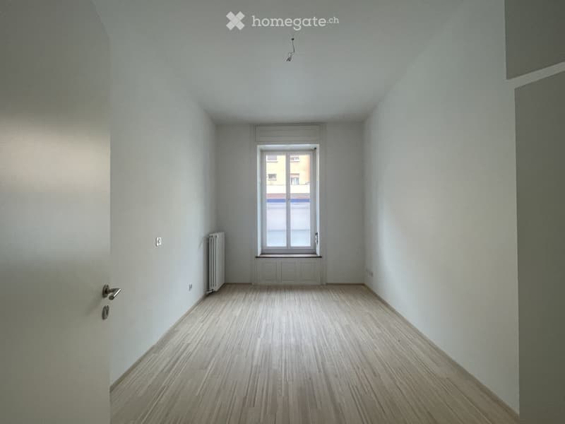 Empty room with light-colored walls, wooden flooring, a single window, and a radiator on one wall.