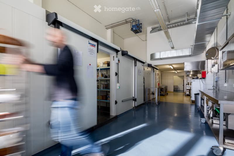Commercial kitchen with stainless steel appliances, refrigerator, counter, sink, and cart.