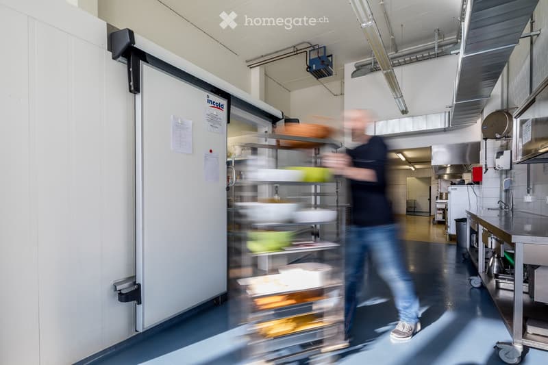 Commercial kitchen with stainless steel appliances, refrigerator, shelves, and a counter.