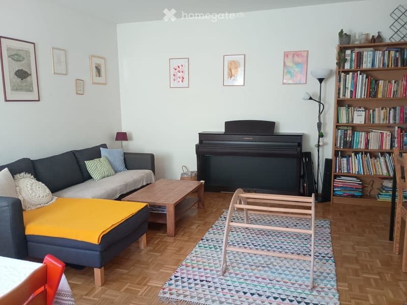 Living room with a dark blue sofa, wooden coffee table, piano, bookshelf filled with books, and a colorful rug on the floor.