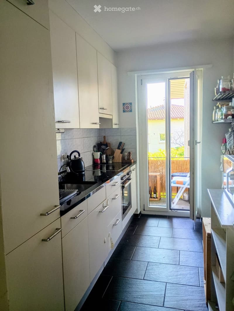 Modern kitchen with white cabinets, stainless steel appliances, and a black countertop. A sliding glass door leads to a patio area.