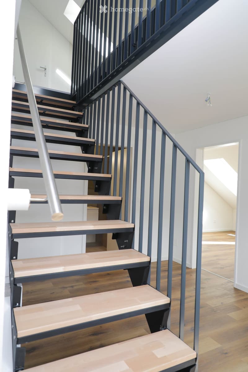 Modern staircase with wooden steps and dark blue railings, leading to an open area with wooden flooring and white walls.