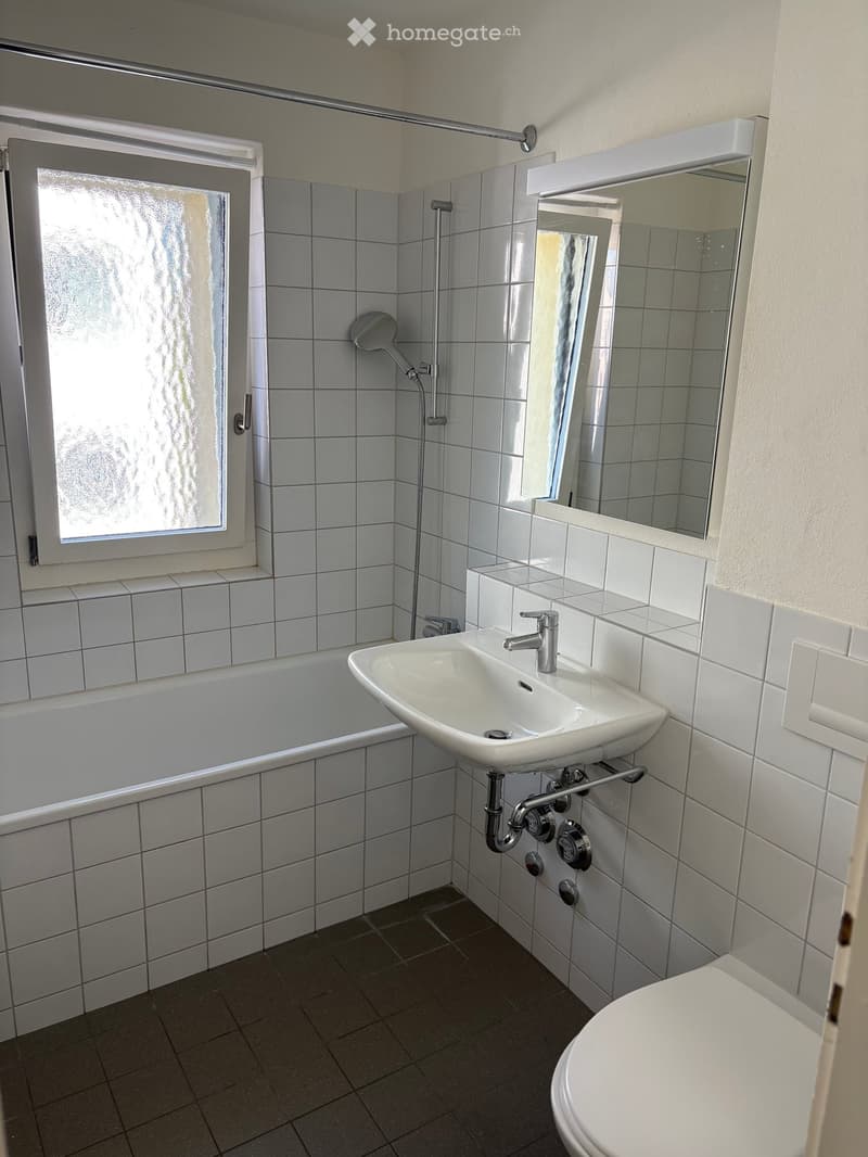 Modern bathroom with white tiles, a sink, toilet, bathtub, and a shower area with a glass door.
