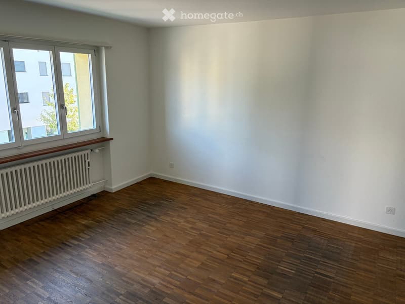 Empty room with wooden flooring, white walls, and a radiator under a window.