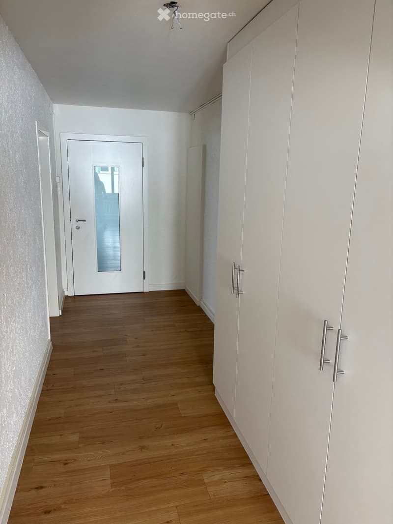 Empty hallway with wooden flooring, white walls, and a white door with a glass panel at the end.