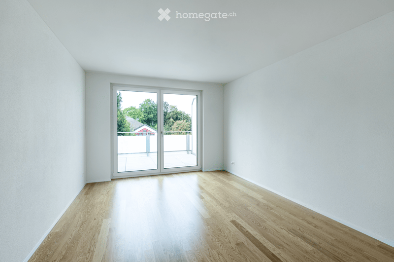 Empty room with light wooden flooring, white walls, and large sliding glass doors leading to a balcony or outdoor area.