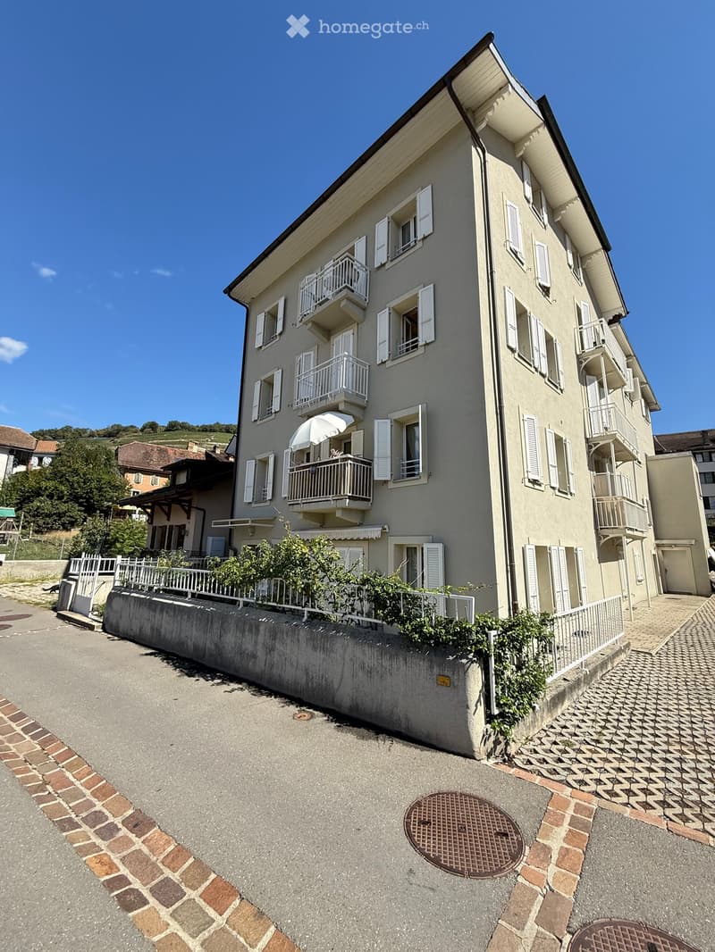 Multi-story residential building with multiple balconies, white shutters, and a raised ground floor.