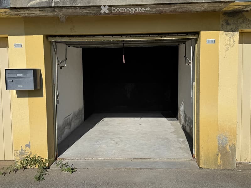 Open garage entrance with yellow walls, concrete floor, and a small mailbox on the left side.