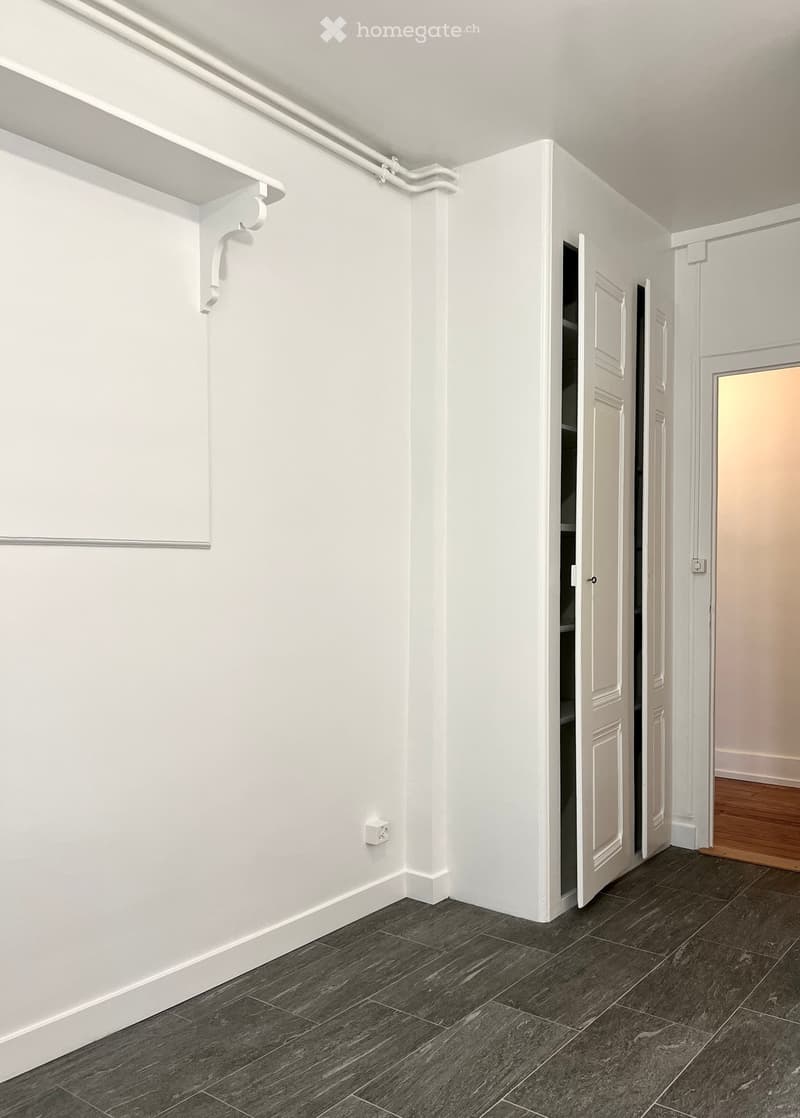 Empty room with white walls, dark grey tiled floor, and white doors. No furniture or equipment visible.