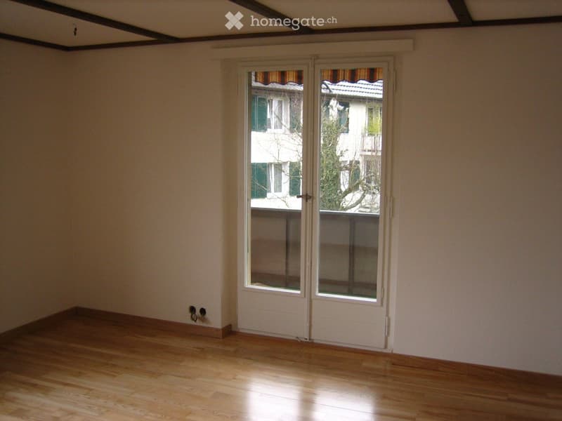 Empty room with wooden flooring, white walls, and a set of double doors leading to a balcony or outdoor area.