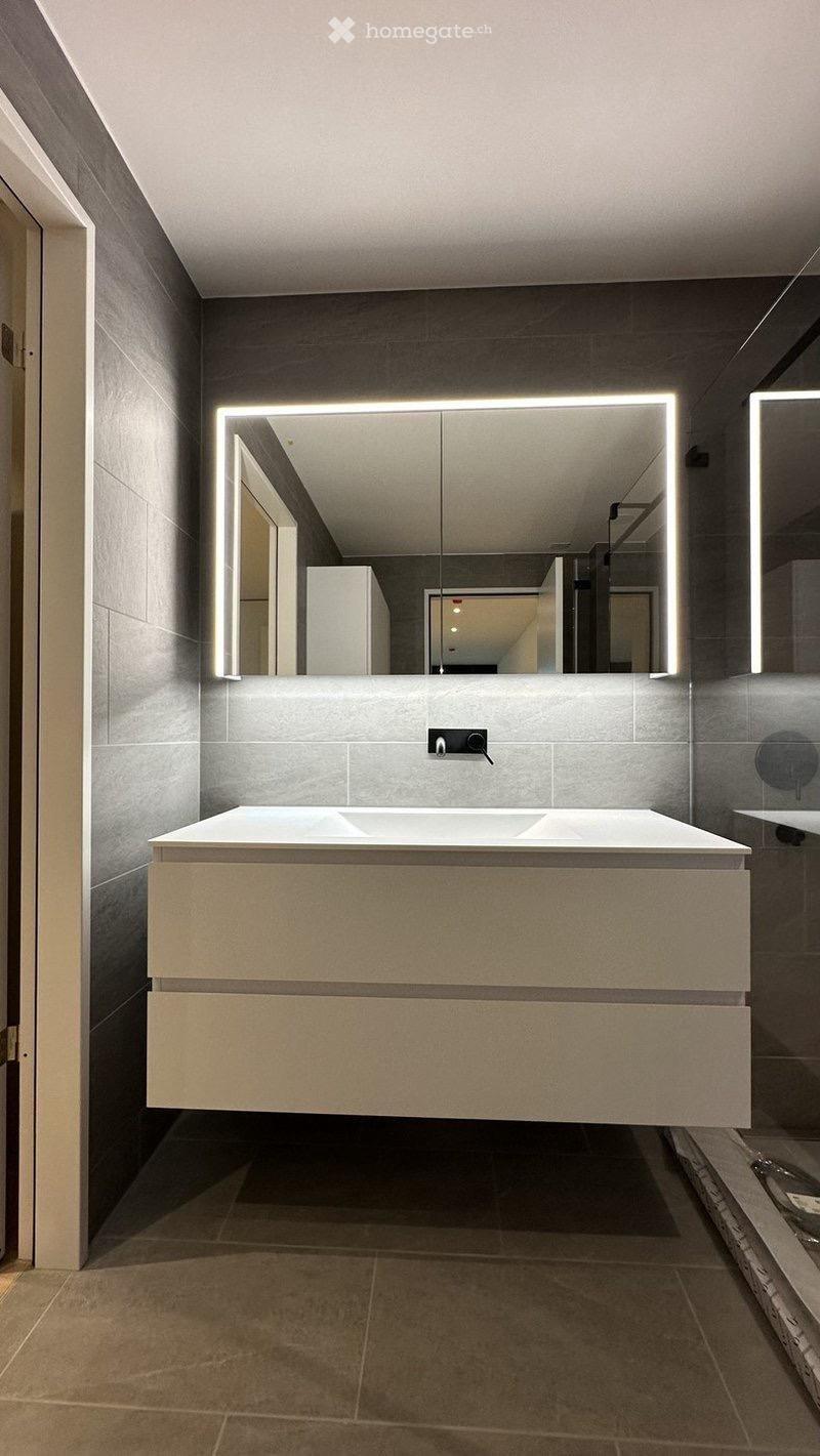 Modern bathroom with a floating vanity, large illuminated mirror, and sleek grey tiles.
